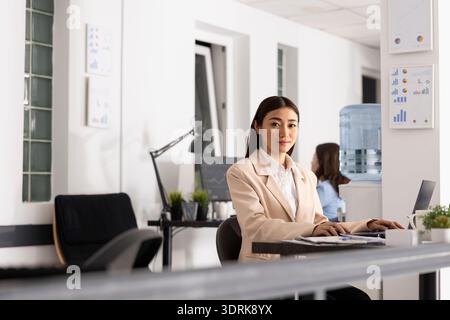 Professionelle Frau sitzt mit Laptop in einem modernen Büro und zeigt, dass sie bereit ist, Geschäftsprojekte und Präsentationen abzuwickeln. Porträt einer asiatischen Buchhalterin, die sich auf den produktiven Arbeitstag vorbereitet. Stockfoto