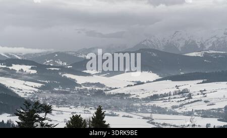 Winterlandschaft eines Dorfes in Podhale mit schneebedeckten Feldern und dem Tatra-Gebirge im Hintergrund, Südpolen Stockfoto