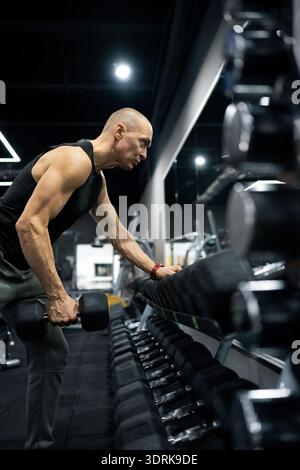 Muskulöser Sportmann, der eine-Arm-Kurzhantelreihenübung im modernen Fitness-Studio durchführt. Krafttraining, Bodybuilding und gesundes Lifestyle-Konzept. V Stockfoto