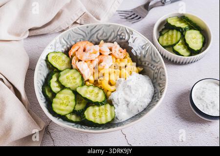 Pasta mit Garnelen, frischer Gurke und cremiger Sauce in einer Schüssel auf dem Tisch Stockfoto