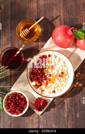 Gesundes Frühstück mit Zutaten. Weicher, körniger Hüttenkäse mit Granatapfelkernen, Rosinen, Honig und Saft auf sonnigem Tisch, Stockfoto