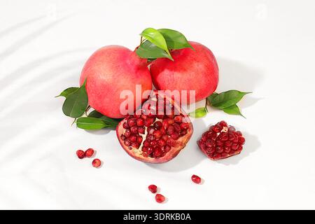 Modernes Stillleben mit Reifen Granatäpfeln und roten Reifen Körnern auf einem hellen Tisch im Schatten von Palmen. Quelle der Vitamine für Stockfoto
