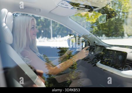 Eine Frau sitzt in einem Auto und hält das Lenkrad, während sie nach vorne blickt. Die Sonne scheint durch die Fenster mit Reflexionen. Stockfoto