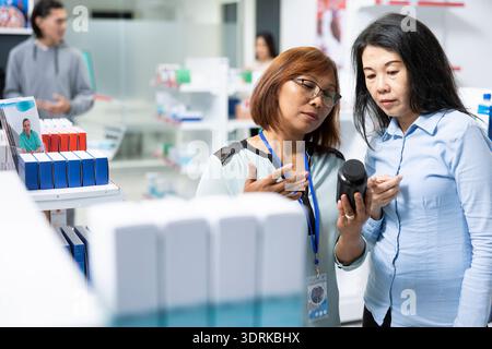 Asiatische Apothekenangestellte bespricht Nahrungsergänzungsmittel und Rezeptoptionen mit Frauen mittleren Alters. Aufmerksamer Kundenservice spiegelt Professionalität, Sorge und Engagement für die Gesundheit der Patienten wider. Stockfoto