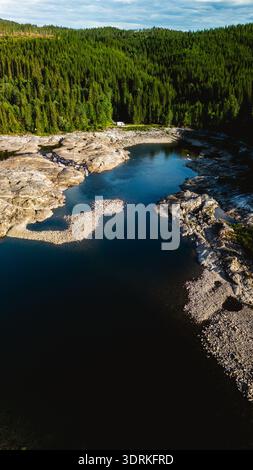 Atemberaubender Blick auf den ruhigen Fluss, der an einem sonnigen Tag durch üppige Wälder in Norwegen fließt Stockfoto