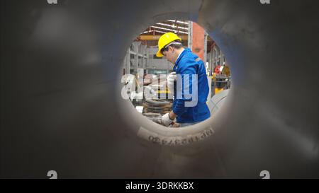 Industriearbeiter, der in einem großen Metallrohr in einer Fabrik inspiziert Stockfoto