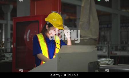 Industriearbeiterin, die in einem großen Metallrohr in einer Fabrik mit Schutzhelm inspiziert Stockfoto