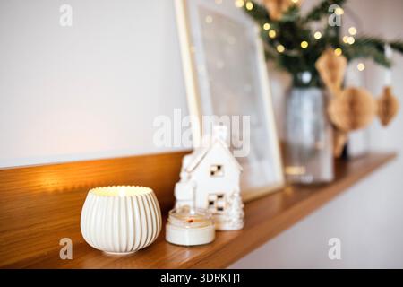 Gemütliches Innenleben mit dekorativer Kerze, einem kleinen Keramikhaus und einem gerahmten Bild auf einem Holzregal, was einen Krieg verursacht Stockfoto