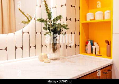 Modernes Badezimmer mit stilvoller Arbeitsplatte mit einer Vase aus Grün, Kerzen und Kosmetikprodukten, ergänzt durch g Stockfoto