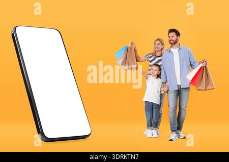 Familie, die ein großes Smartphone mit leerem Bildschirm auf orangem Hintergrund sieht. Tochter zeigt auf Gerät Stockfoto