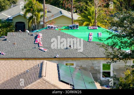 Asphaltschindeln werden auf dem neuen Hausdach aufgebracht. Dachdecker sichern Schindeln. Wohnbaustelle in Florida. Stockfoto