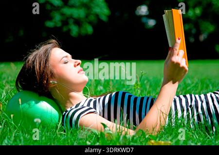 Eine junge Frau, die auf einer Wiese liegt und ein Buch liest Stockfoto