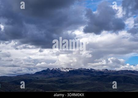 Eine zerklüftete Bergkette in Peru, teilweise mit Schnee bedeckt, liegt unter einem dramatischen Himmel voller dunkler Sturmwolken und Patschen Stockfoto