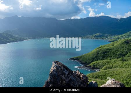 Die Taiohae Bay in Nuku Hiva, Marquesas Inseln, ist von grünen Bergen unter einem blauen und bewölkten Himmel umgeben, mit Segelbooten vor Anker Stockfoto