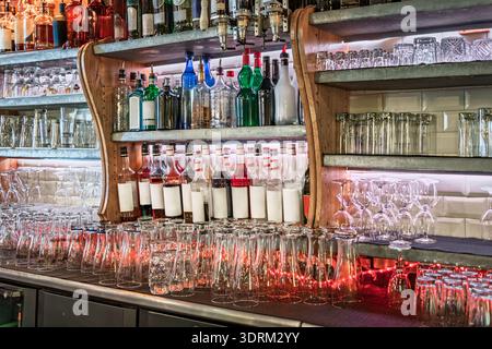 Glasreihen und farbenfrohe Flaschen mit Spirituosen und Sirupe stehen auf Holzregalen in einer gemütlichen Bar in der Altstadt oder Vieille Ville von Nizza, Frankreich Stockfoto