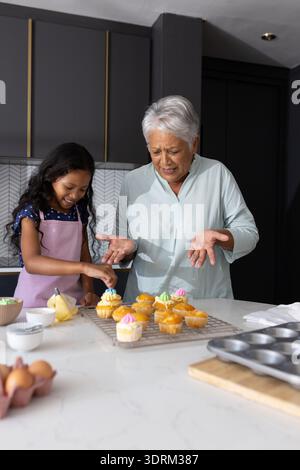 Cupcakes dekorieren, Großmutter und Enkelin lachen in der modernen Küche. Backen, Familie, Generationen, Binden, Kuh Stockfoto