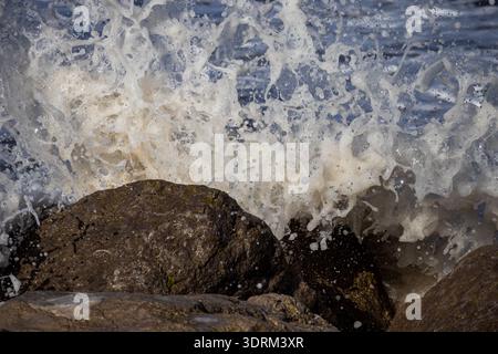 Mächtige Meereswellen, die mit weißem Sprühnebel und Schaum gegen Küstenfelsen krachen Stockfoto