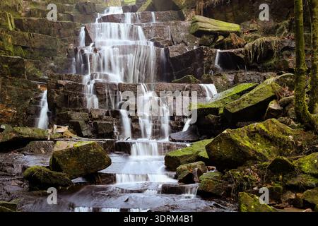 Gestufter Waldwasserfall, der über moosige Felsen fließt, mit langer Exposition in einer ruhigen Waldumgebung erfasst. Stockfoto