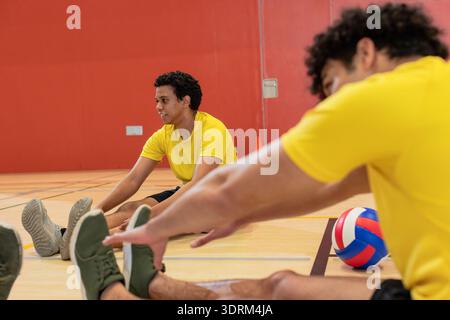 Afroamerikanische Teamkollegen, die ihre Beine auf dem Fitnessboden mit Volleyball, Kegeln und Kopierraum Strecken. Athleten, Fitness, Training, Sport, Stockfoto