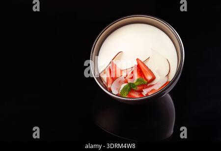 Köstliches Dessert mit Erdbeeren und Creme, serviert in einer einfachen schwarzen Schüssel auf dunklem Hintergrund Stockfoto