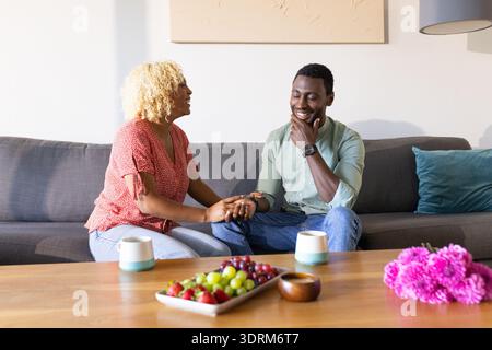 Freunde, die sich auf dem Sofa unterhalten und bei Kaffee und Snacks lachen. Freundschaft, Verbundenheit, Zusammenkommen, Freizeit, Entspannung Stockfoto