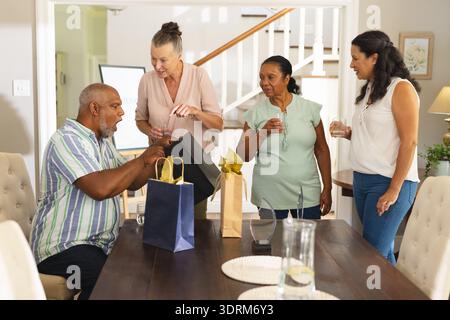 Geschenktüte öffnen, Seniorenmann umgeben von Freunden, die zusammen zu Hause feiern. Feier, Party, Versammlung, Glück, Frien Stockfoto