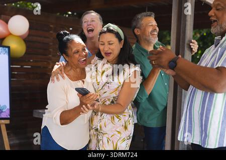 Senioren feiern gemeinsam im Freien, lachen und teilen Momente mit dem Smartphone. Ältere Menschen, Technologie, Glück, Freundschaft, Stockfoto