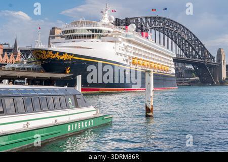 Eine rivercat Fähre und Disney Wonder Cruiseliner liegen neben der Sydney Harbour Bridge an, während ihre Passagiere die malerische Aussicht auf den Hafen von Sydney genießen. Stockfoto