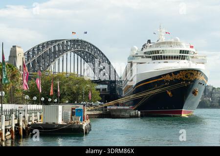 Das luxuriöse Cruiseliner Disney Wonder liegt neben der Sydney Harbour Bridge, während Touristen die Sehenswürdigkeiten und die Unterhaltung am Circular Quay genießen. Stockfoto