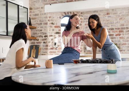 Lachen und teilen sich die Momente, drei junge Frauen versammeln sich in einer gemütlichen Küche. Freundschaft und Freude erfüllen Luft, wenn sie sich gegenseitig amüsieren Stockfoto