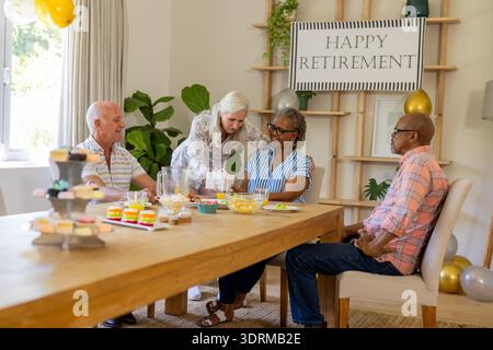 Seniorenfreunde feiern den Ruhestand mit Snacks und Lachen zu Hause. Feier, Freundschaft, Glück, Gruppe, lei Stockfoto