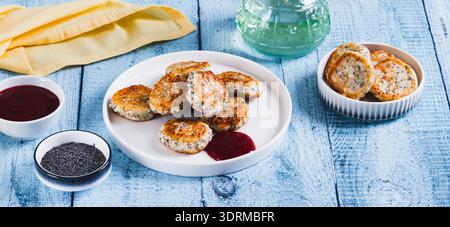 Mini-Hüttenkäse-Pfannkuchen mit Mohn und Beerenmarmelade auf einem Teller auf dem Tischwebbanner Stockfoto