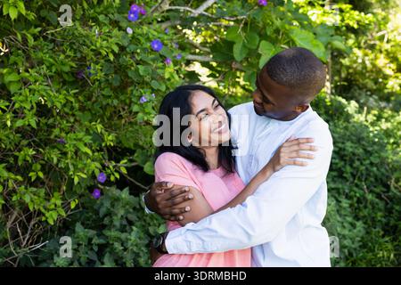 Ein Paar, das sich fröhlich im Garten umgibt und die Liebe inmitten von lebendigem Grün feiert. Romantik, Beziehung, Zuneigung, Glück, Outdoor, Natur Stockfoto