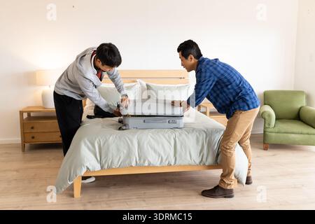 Zwei Männer packen Koffer ins Bett und bereiten sich auf die Reise nach Hause vor. Urlaub, Vorbereitung, Gepäck, Abenteuer, Reise, Entspannung Stockfoto