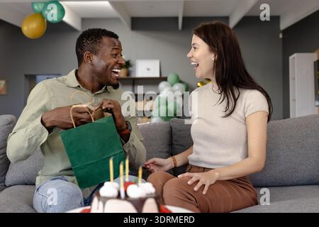 Geschenke austauschen, glückliches Paar feiert Geburtstag mit Kuchen und Ballons zu Hause. Feiern, Liebe, Romantik, Gegenwart, glücklich Stockfoto