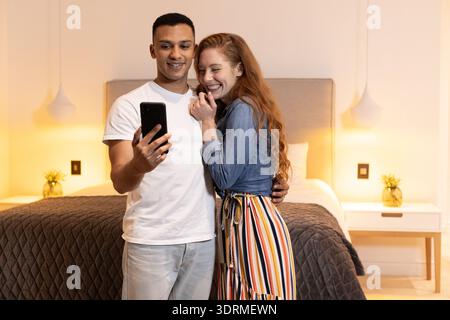 Junges Paar macht Selfie zusammen im gemütlichen Schlafzimmer, lächelt und genießt den Moment. Glück, Zweisamkeit, Lebensstil Stockfoto