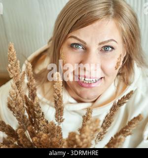 Lächelnde kaukasische reife Frau mit blondem Haar, die getrocknete Grasstämme hält Stockfoto