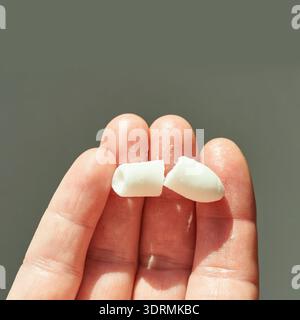 Nahaufnahme einer Hand, die gebrochene weiße Kaugummistücke vor grauem Hintergrund hält Stockfoto