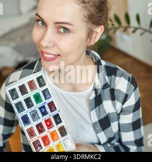 Junge kaukasische Künstlerin mit Aquarellpalette im zwanglosen Heimstudio Stockfoto