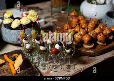 Rustikales Partybuffet auf einem Holztisch mit Mini-Burger-Schiebern auf einem Servierbrett und kleinen Stielgläsern gefüllt mit Pesto und Kirschtoma Stockfoto