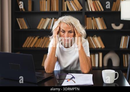 Kopfschmerzen. Frau mittleren Alters, die Schläfe berührt und Stress erlebt. Reife alte Dame müde der Arbeit, Kopfschmerzen, krankes Rubbi Stockfoto