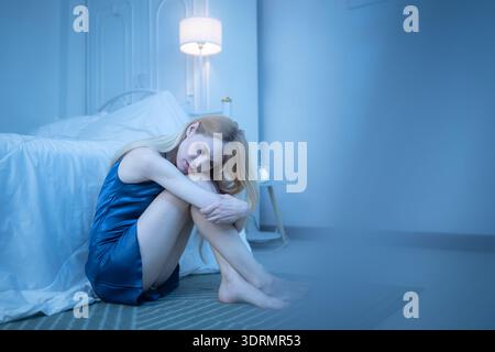 Eine junge Frau im blauen Pyjama fühlt sich traurig, nachdem sie Informationen von ihrem Handy erhalten hat Stockfoto
