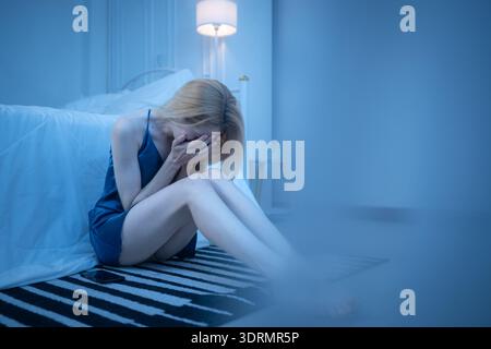 Eine junge Frau im blauen Pyjama fühlt sich traurig, nachdem sie Informationen von ihrem Handy erhalten hat Stockfoto