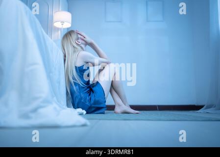 Eine junge Frau im blauen Pyjama fühlt sich traurig, nachdem sie Informationen von ihrem Handy erhalten hat Stockfoto