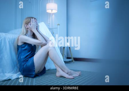 Eine junge Frau im blauen Pyjama fühlt sich traurig, nachdem sie Informationen von ihrem Handy erhalten hat Stockfoto