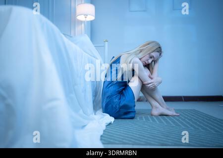 Eine junge Frau im blauen Pyjama fühlt sich traurig, nachdem sie Informationen von ihrem Handy erhalten hat Stockfoto
