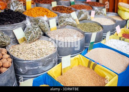Farbenfrohe Auswahl an Gewürzen und Kräutern, die in Metallbehältern und gewebten Körben auf einem lebhaften Markt präsentiert werden und die Vielfalt präsentieren Stockfoto