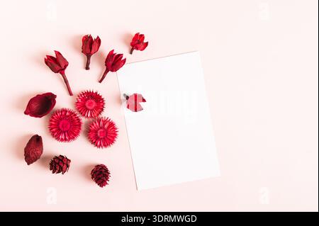 Leeres Blatt zum Schreiben und trockene rote Blumen auf rosafarbenem Hintergrund Draufsicht Stockfoto