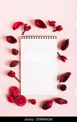 Notizbuch zum Schreiben in einem Rahmen aus getrockneten roten Blumen auf rosafarbenem Hintergrund oben und vertikal Stockfoto