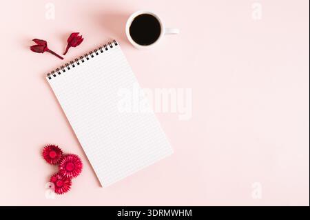 Notizbuch zum Schreiben, Tasse Kaffee und trockene rote Blumen auf rosa Hintergrund von oben Stockfoto